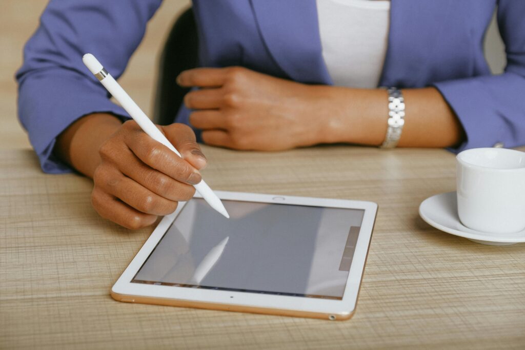 African American woman using a stylus on a tablet at a desk, with coffee nearby.