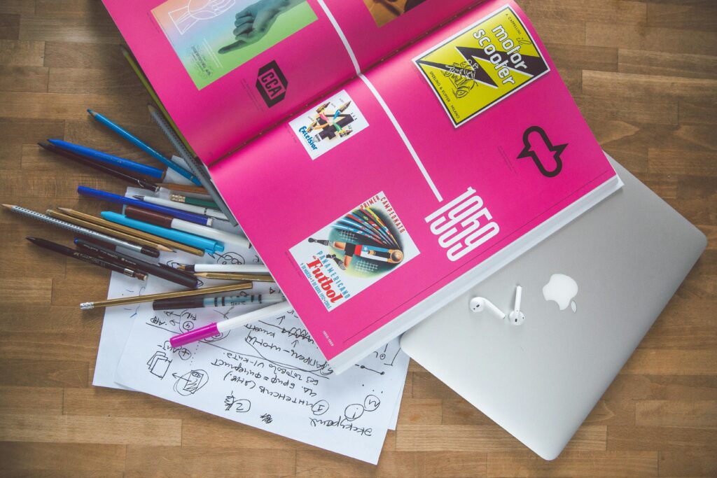 A bright desk setup featuring a design book, laptop, and creative tools, ideal for inspiration.