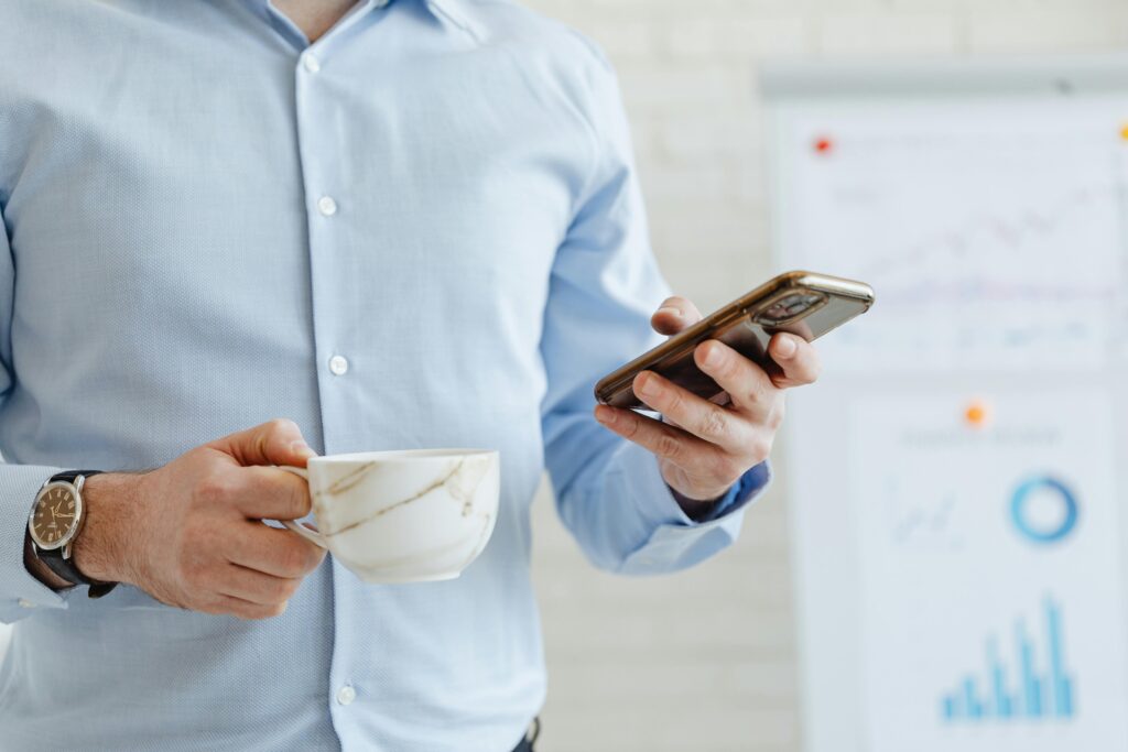 A business professional holding a coffee cup while checking a smartphone in a corporate setting.