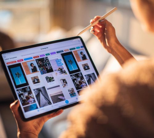 A person uses a digital tablet with a stylus indoors in a warm, cozy setting.