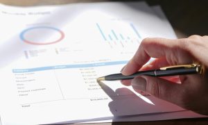 Hand holding pen, analyzing budget with charts and graph paper.