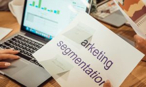 A modern workspace showing hands analyzing marketing data on a laptop and paper documents.